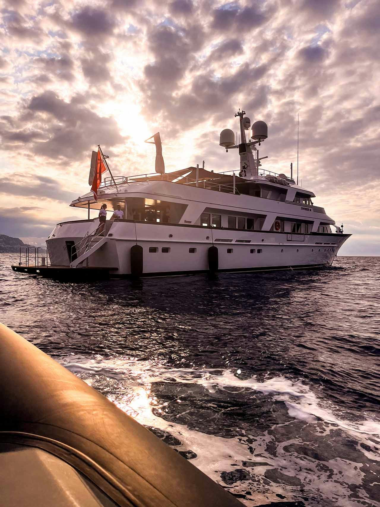 A classic yacht at anchor viewed from its tender at sunrise with an overcast sky overhead