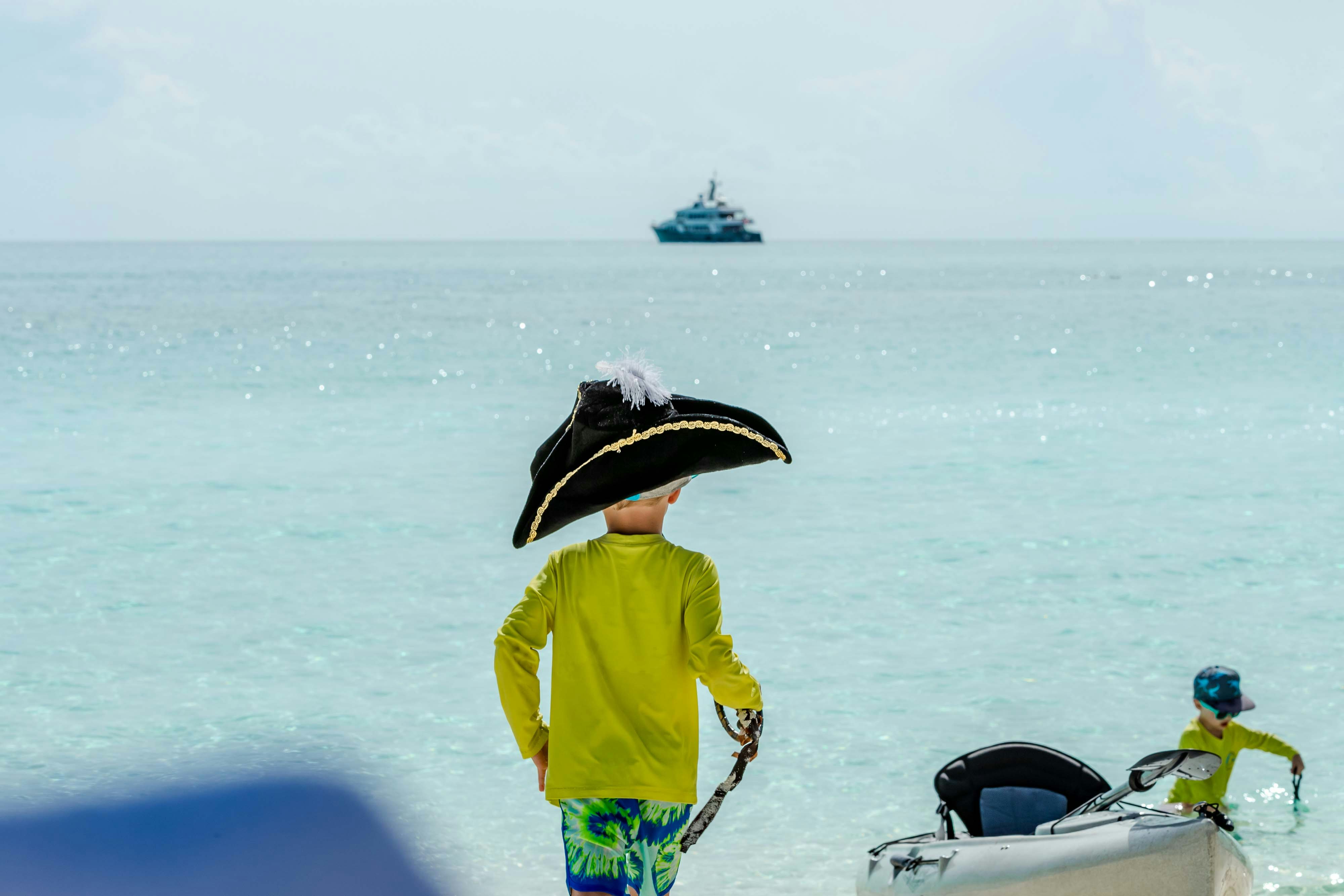 Shadowl kids playing pirate on beach with a yacht in the background