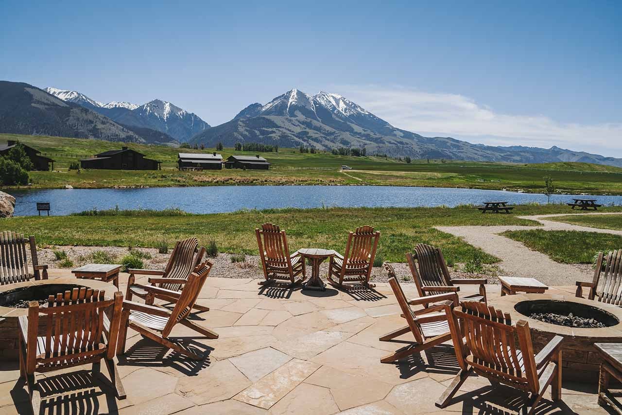 Wooden tables and chairs in front of a small lake with mountains in the background