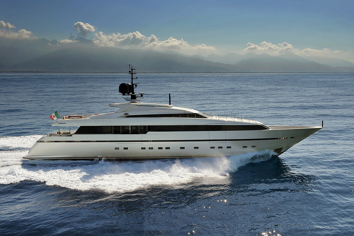 The Sanlorenzo 40 Alloy yacht, with the Italian flag, glides through blue waters with a mountain range in the background, available for sale through Northrop & Johnson.
