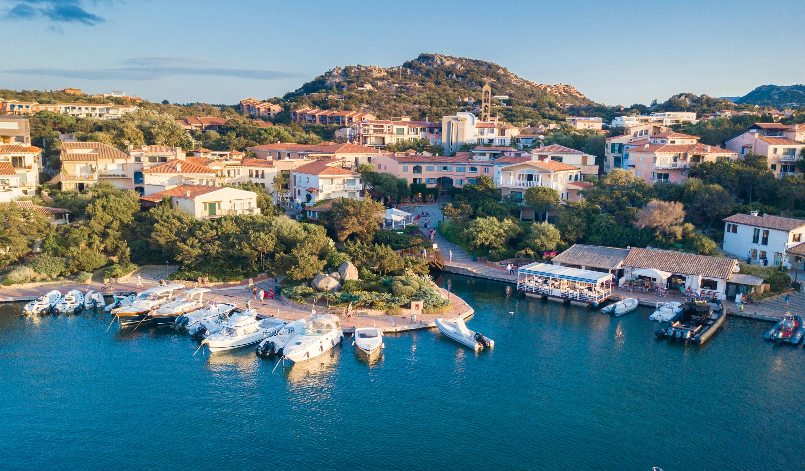 Sardinian Marina Elegance - Premier Yachting with N&J Aerial perspective of a Sardinian marina with yachts docked in crystal-clear waters.