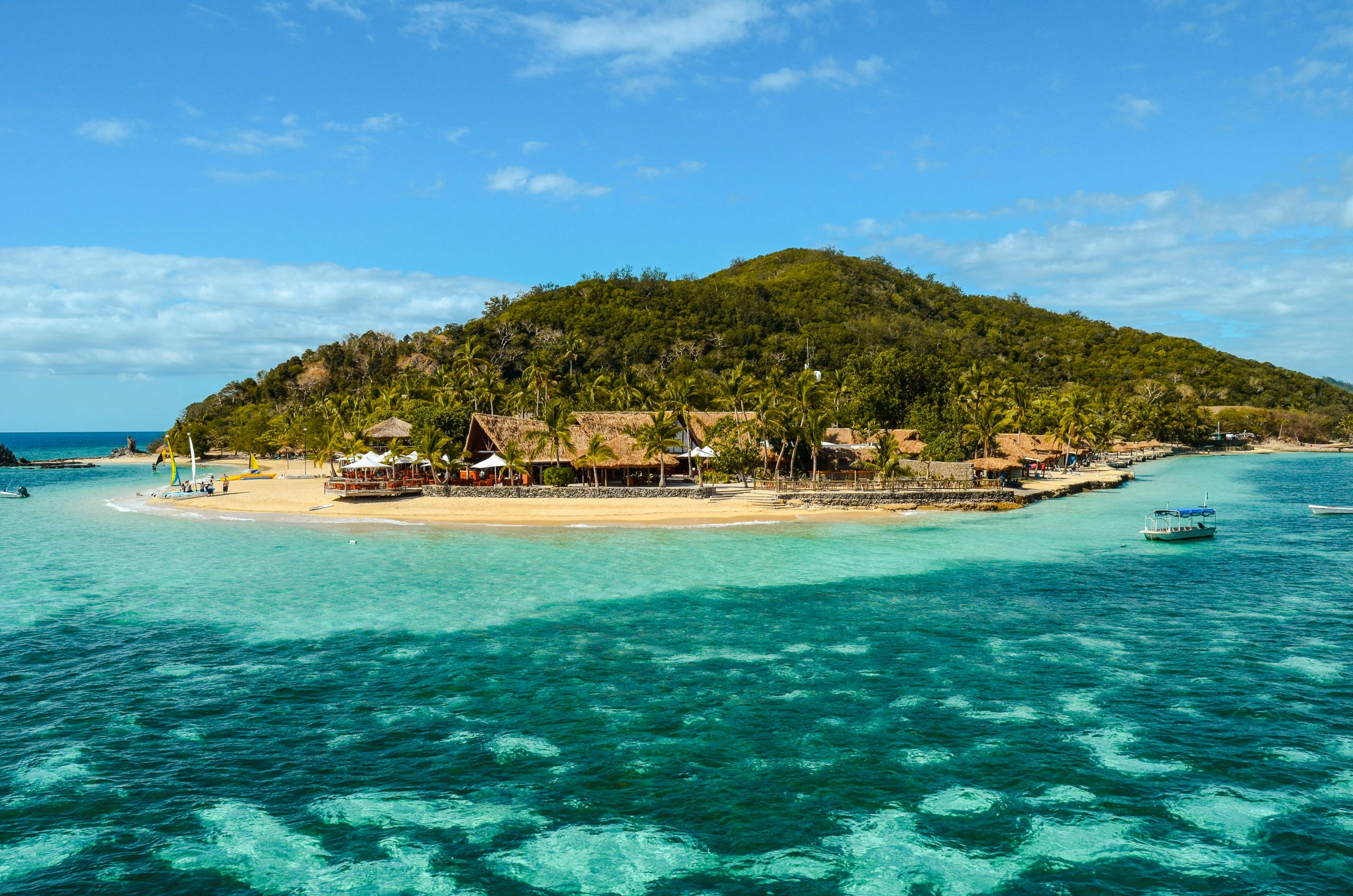 A small Fijian island with traditional thatched huts surrounded by clear turquoise waters.