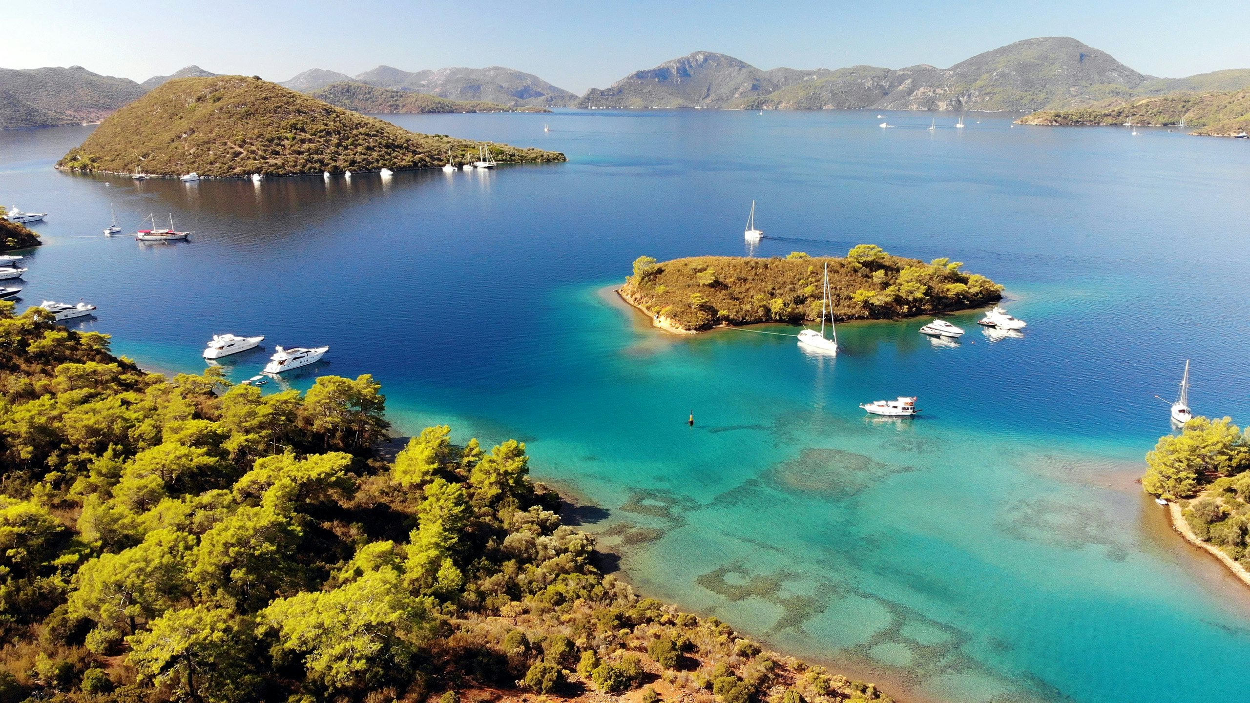 Yachts surrounding a verdant island in the vibrant blue waters of the Turkish Aegean.
