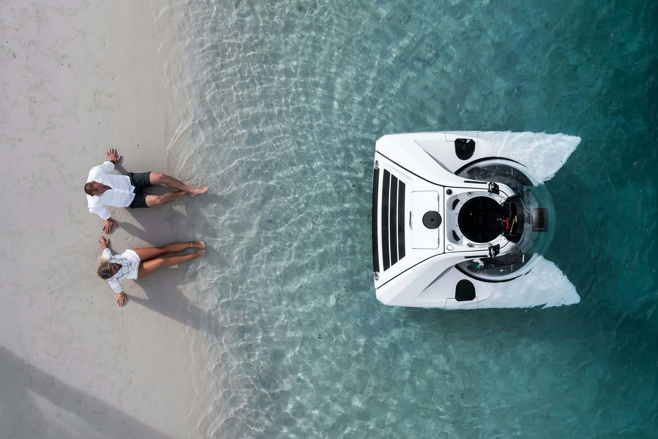 U Boat Worx NEMO submarine for two people with a man and a woman sitting on the sand of an island