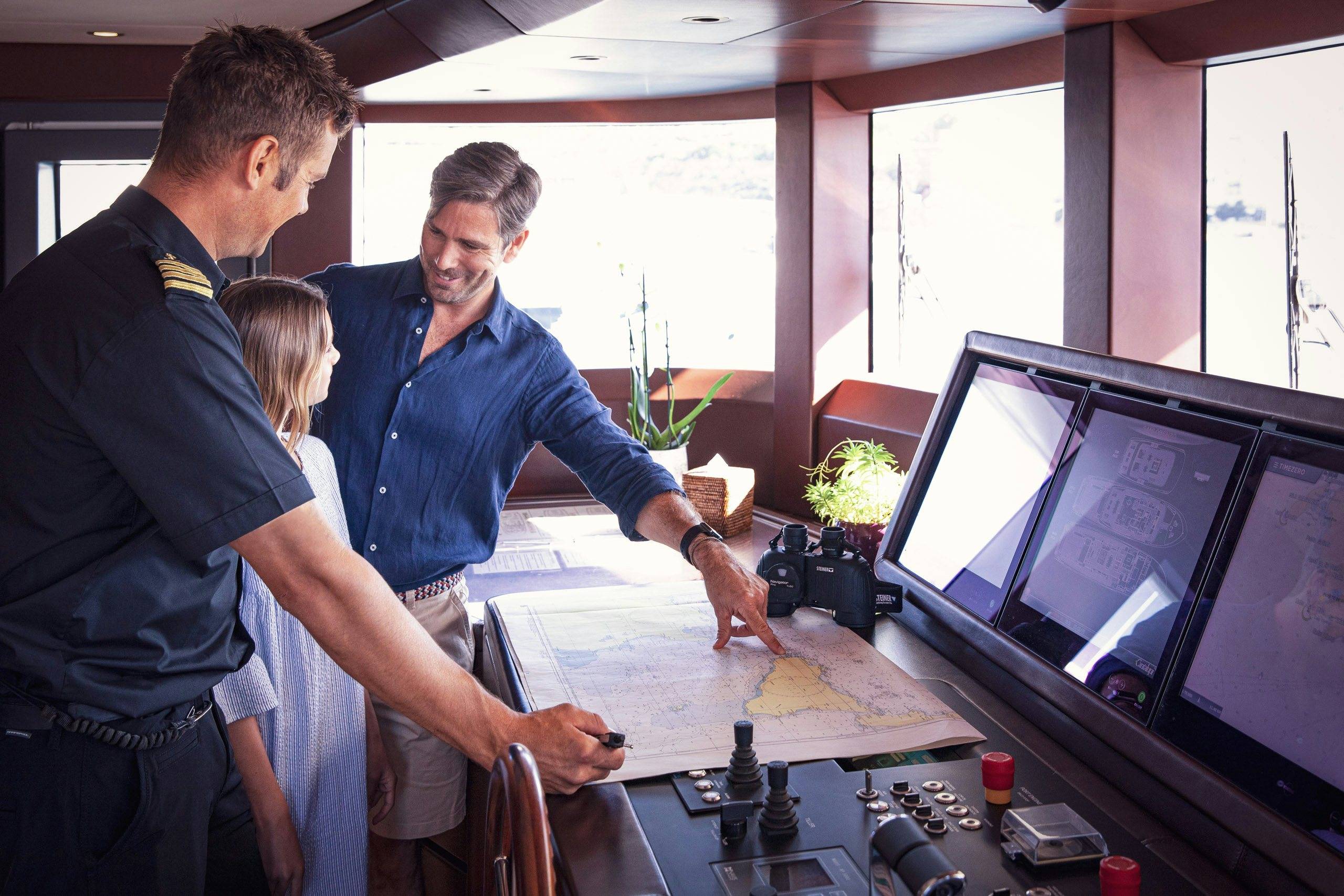 Father and daughter looking at map with the captain on board yacht during crewed yacht charter Father and daughter looking at map with the captain on board yacht during crewed yacht charter