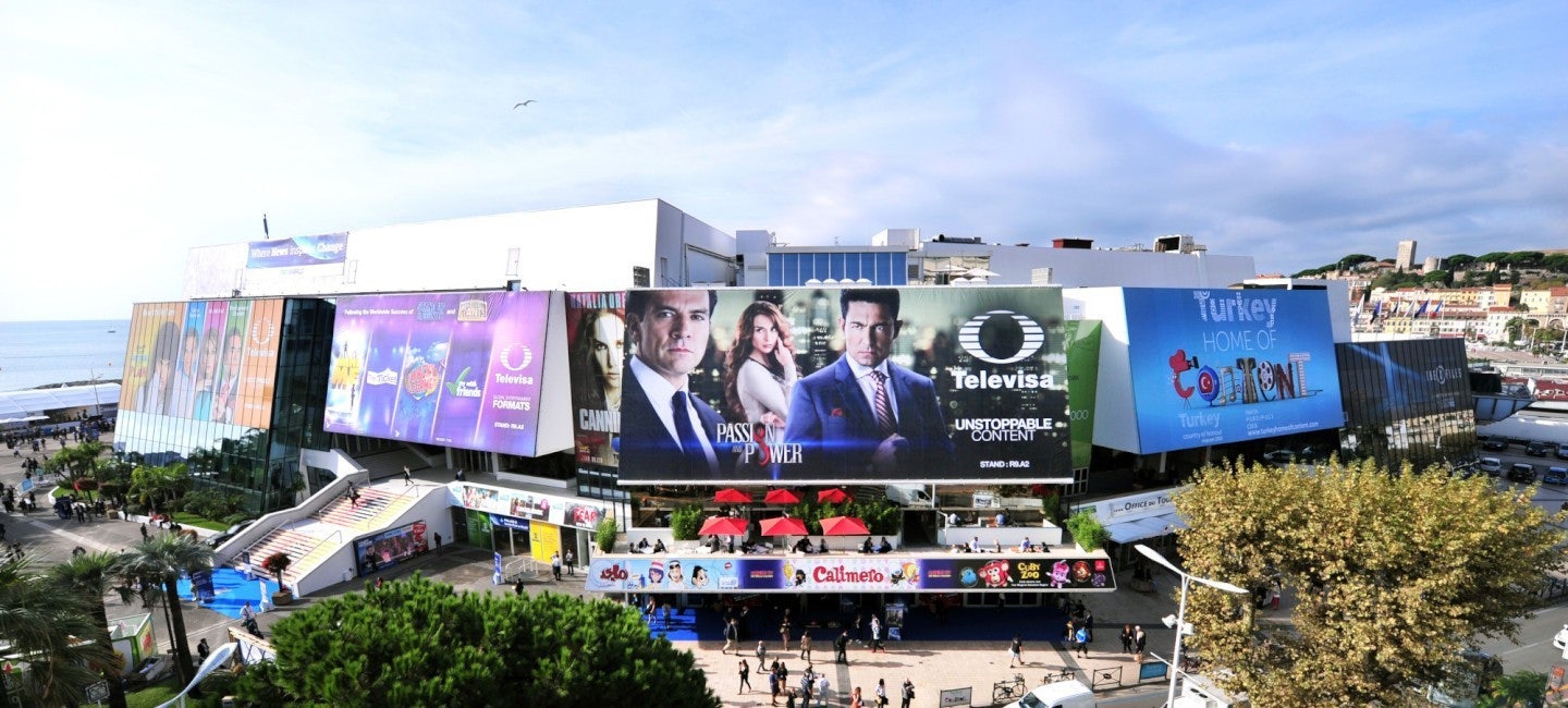 A picturesque view of the Palais des Festivals in Cannes, illuminated by the sun, with people entering the venue to attend MIPCOM 2024.