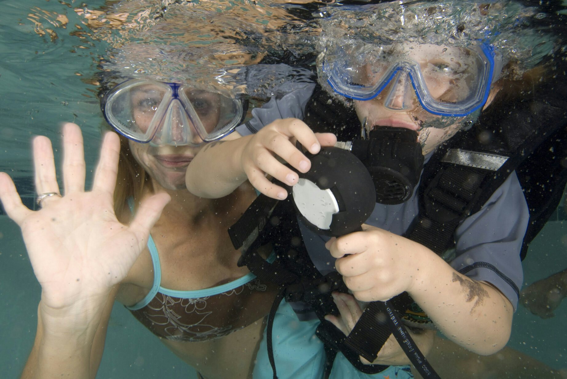 Two kids in masks underwater playing with a regulator