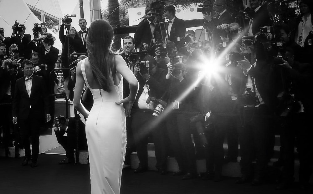A moment of pure elegance as an actress walks the Cannes Film Festival red carpet, illuminated by the flashing cameras of photographers capturing her captivating presence.