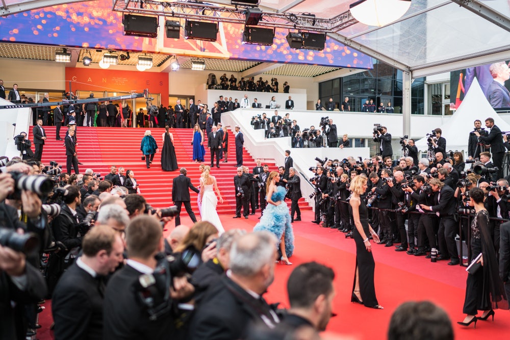 A scene of opulence as VIPs arrive at the main entrance of the Cannes Film Festival, stepping onto the iconic red carpet, surrounded by the allure of glamour and flashing cameras.