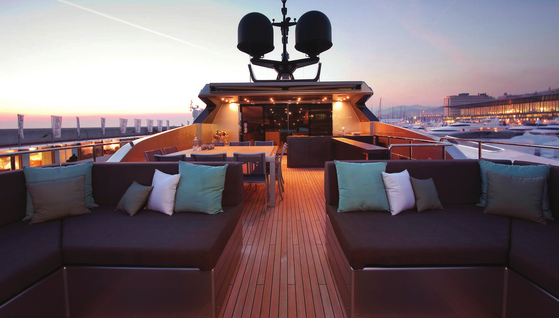 The aft deck of the Sanlorenzo 40 Alloy yacht during twilight, featuring plush seating with soft lighting, against a marina backdrop.