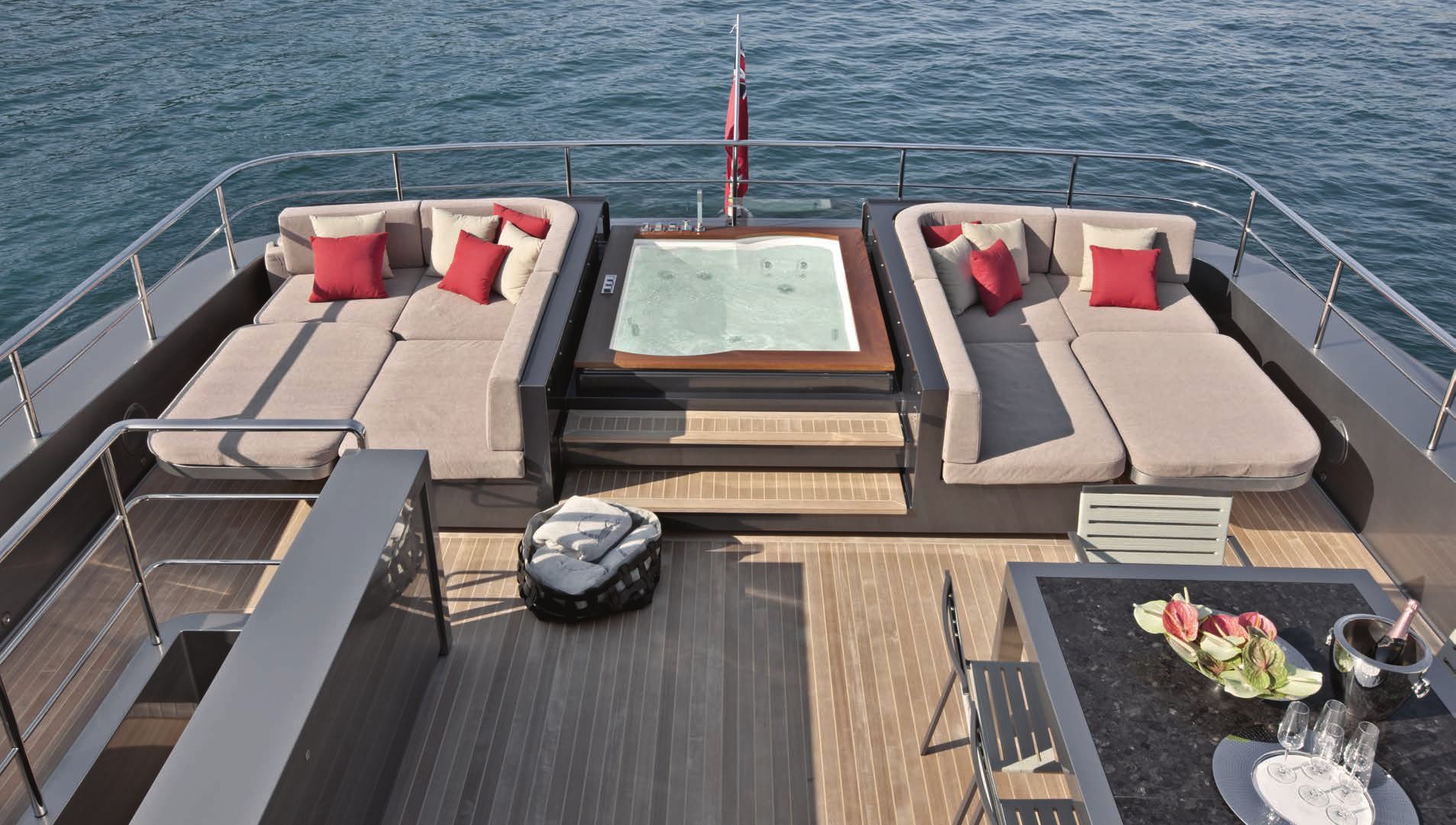 A luxury jacuzzi on the deck of the Sanlorenzo 40 Alloy yacht, flanked by plush lounges with red accent pillows, ready for relaxation.