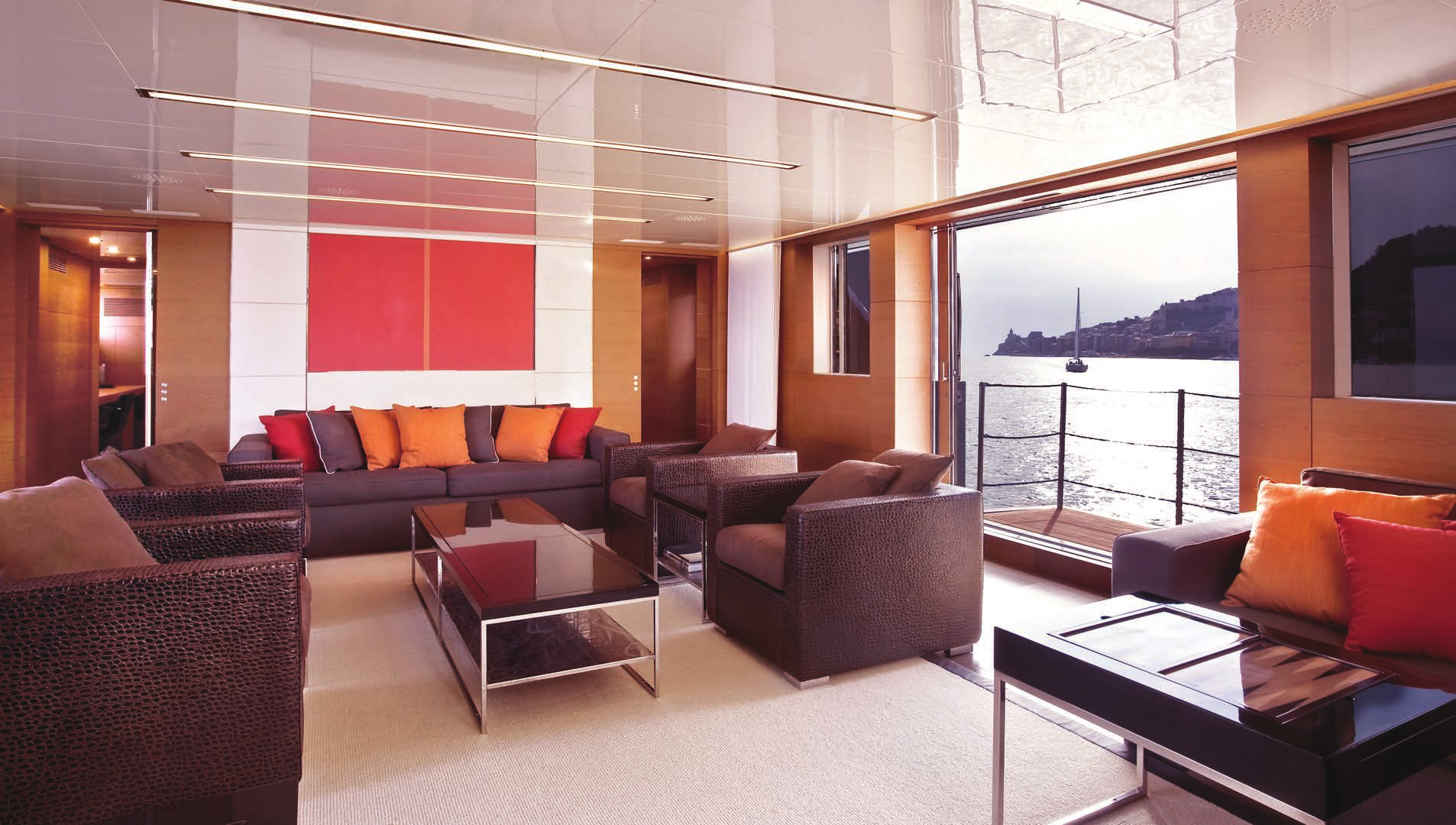 Lounge area inside the Sanlorenzo 40 Alloy yacht for sale with N&J, showcasing dark wicker furniture, orange cushions, and a red art piece.