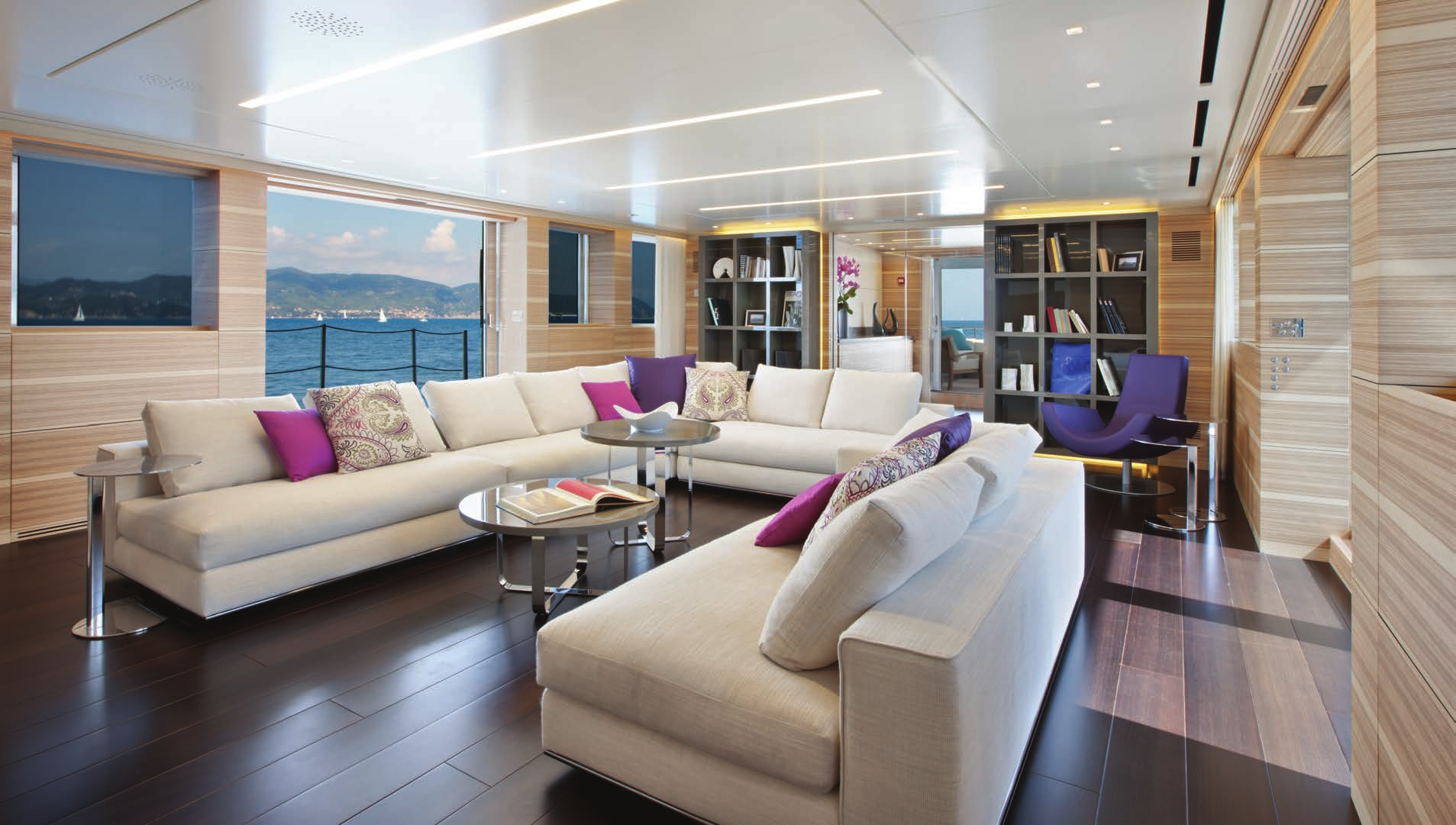 Upper deck salon on the Sanlorenzo 40 Alloy for sale at N&J, with a chic sectional sofa, purple accents, and ocean vistas.