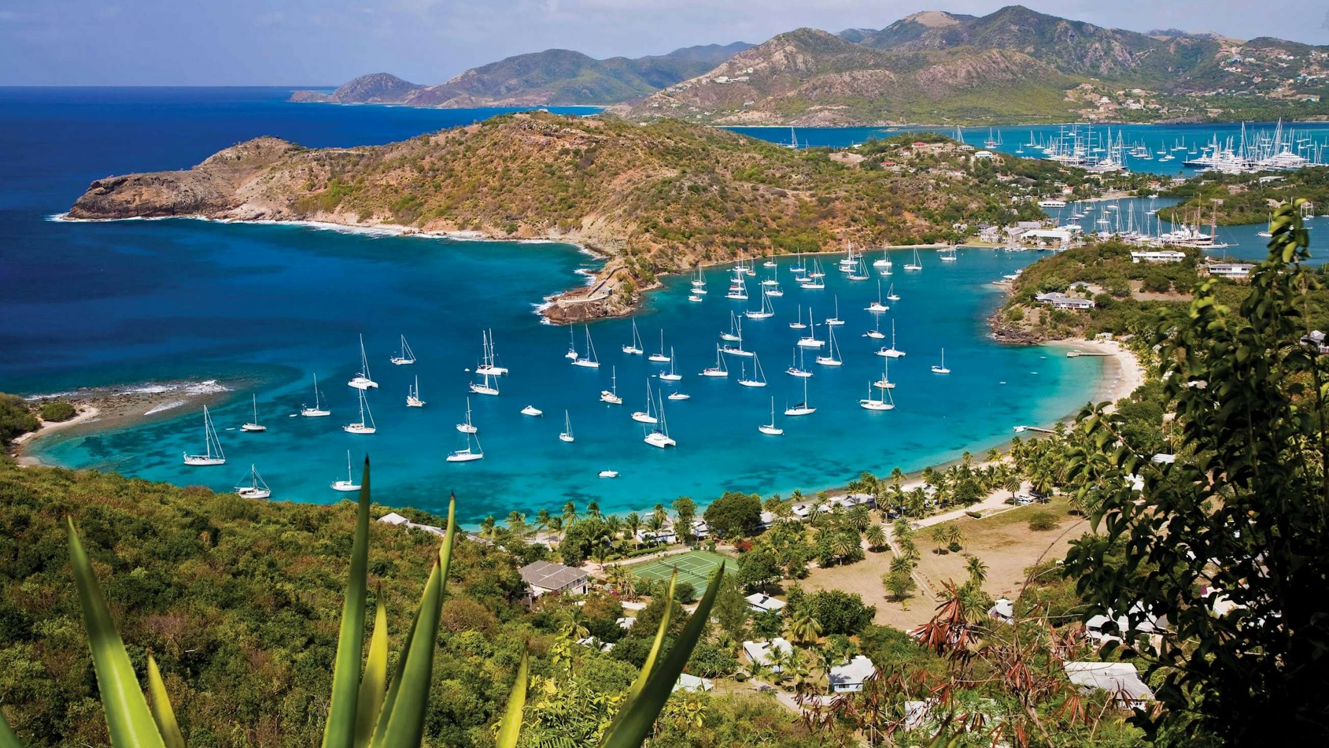 A stunning view from the top of Shirley Heights in Antigua, showcasing the vibrant harbor, anchored boats, and the sparkling sea—a captivating scene for your Antigua Yacht Experience.