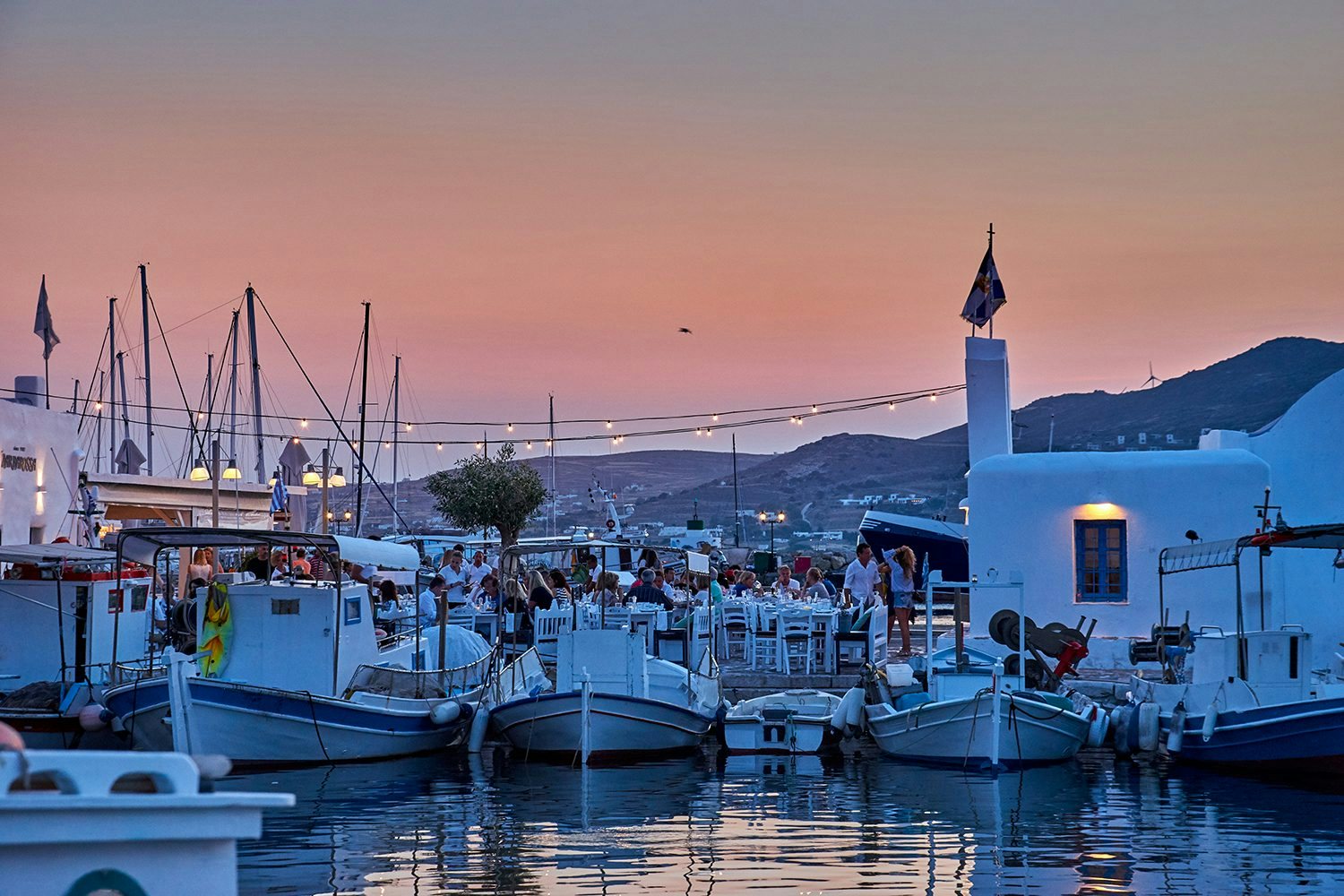 Luxury yachts docked in a Greek marina, basking in the glow of a stunning sunset, ready for a night of elegance.