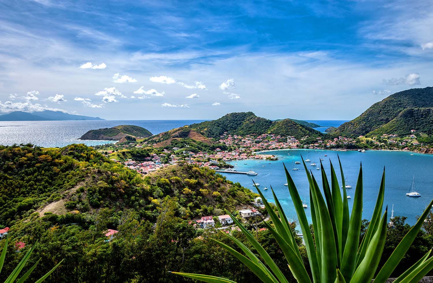 scenic image of Guadeloupe, lush greenery backed by turquoise waters and yachts at anchor, idyllic Caribbean destination