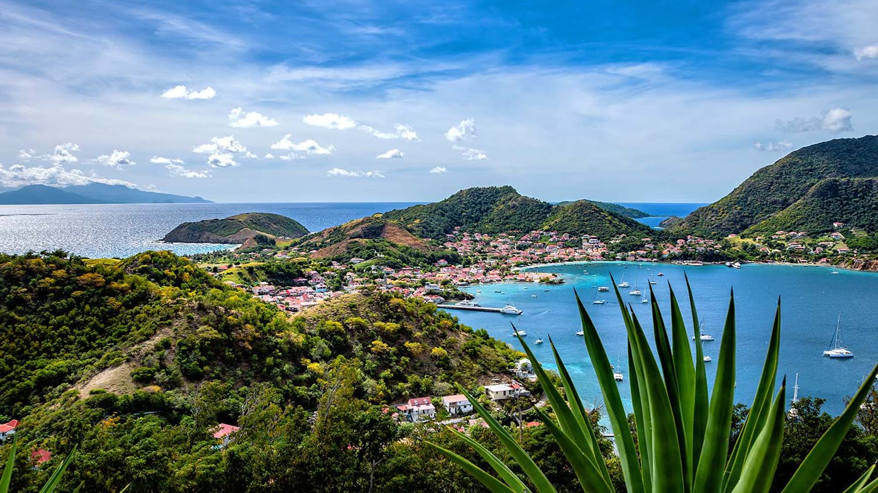 scenic image of Guadeloupe, lush greenery backed by turquoise waters and yachts at anchor, idyllic Caribbean destination
