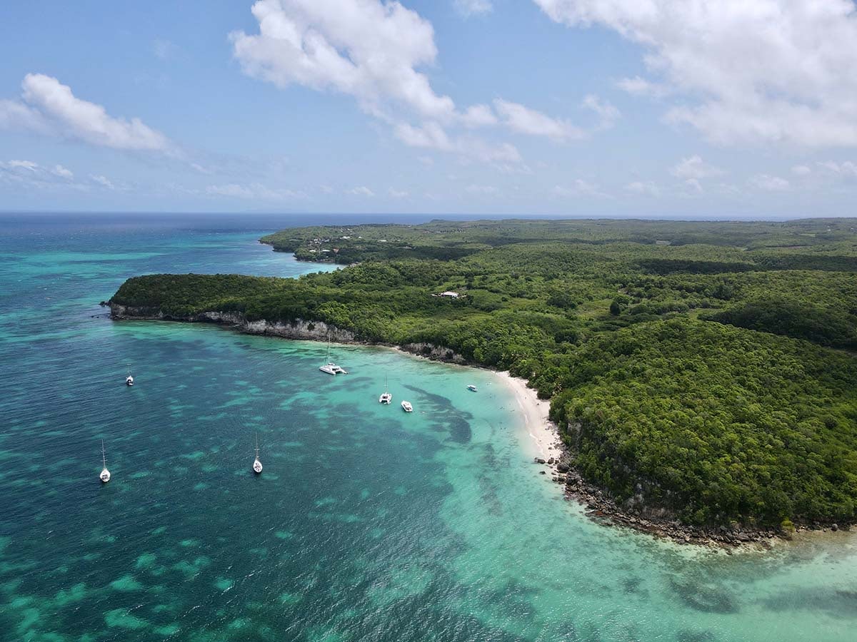 scenic image of Guadeloupe, lush greenery backed by turquoise waters and yachts at anchor, idyllic Caribbean destination
