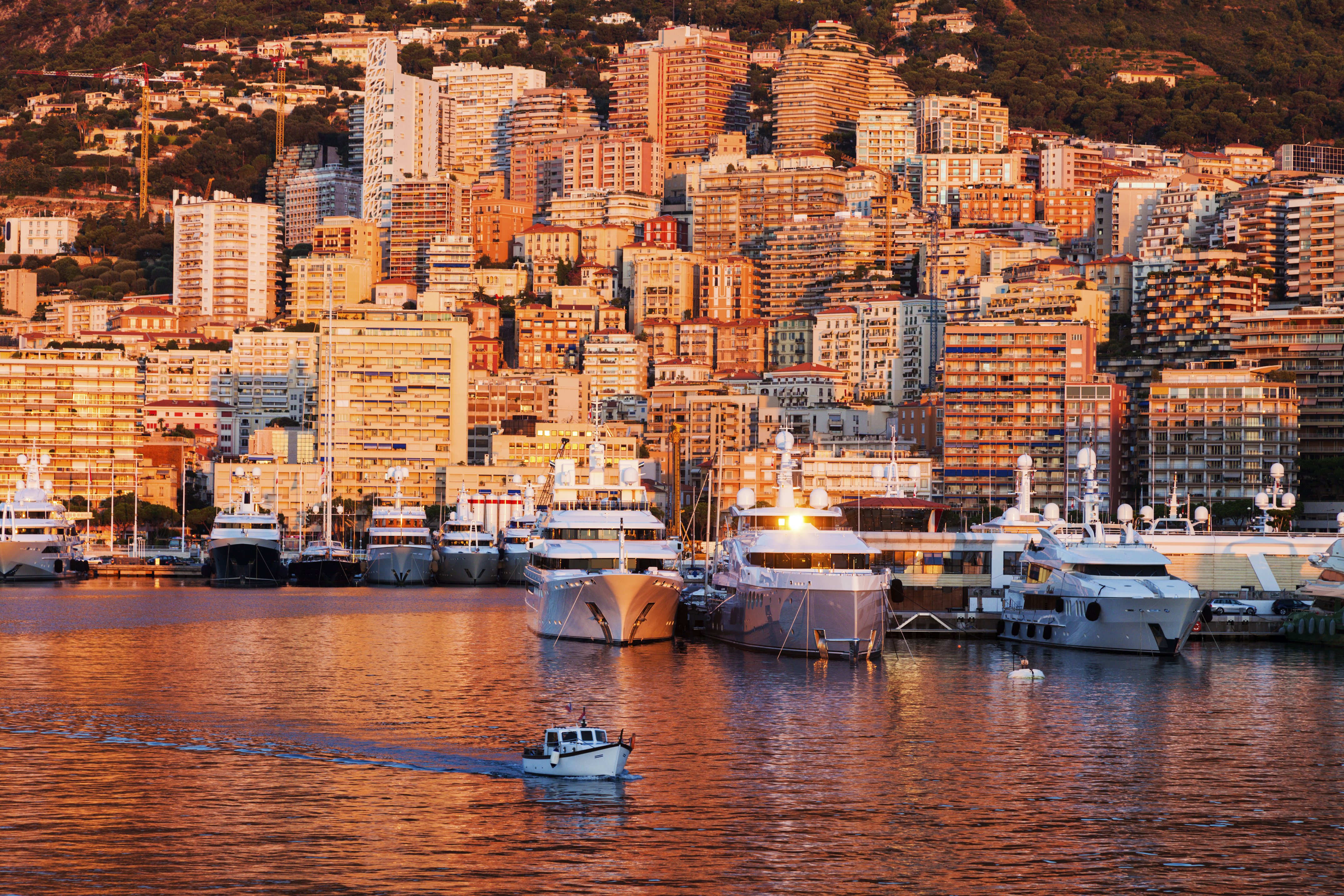 A breathtaking view of Port Hercule in Montecarlo bathed in the warm hues of a sunset, with magnificent superyachts on display during the Monaco Yacht Show.