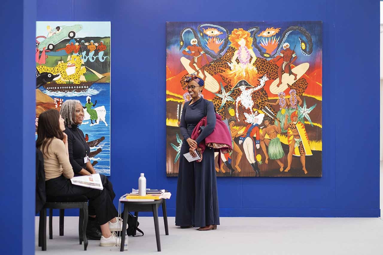 Three women in a gallery with electric blue walls, standing in front of bright artworks